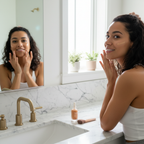 Woman with medium warm golden skin tone applying lightweight tinted foundation, radiant complexion, modern marble bathroom