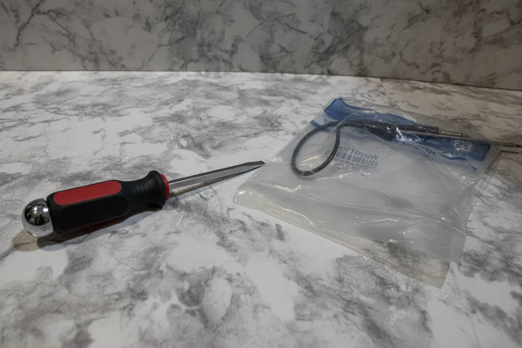 Screwdriver resting on granite counter next to new OEM oven replacement parts