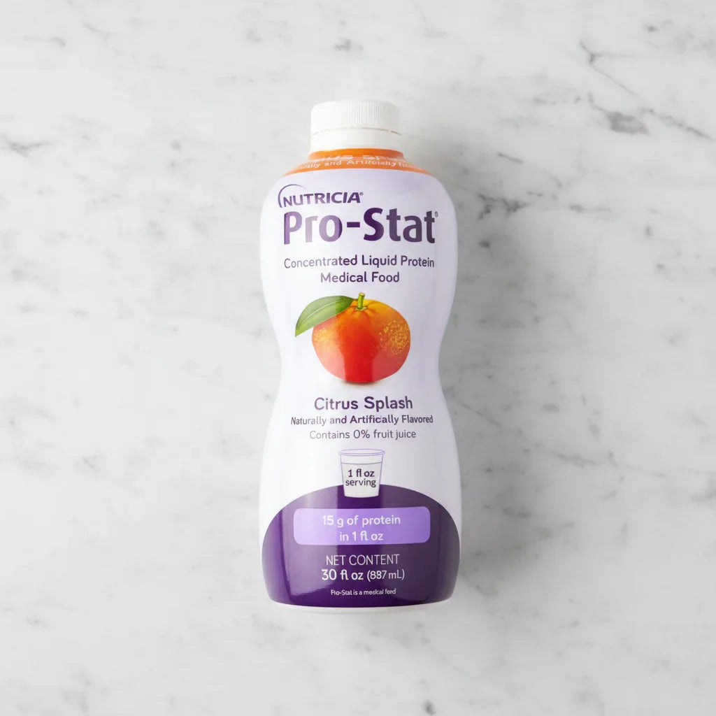 Overhead flat lay of Nutricia Pro-Stat liquid protein medical food bottle on white marble surface, bright even studio lighting