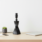 Modern desk display with matte black twisted lamp base against clean neutral tones and light wood surface