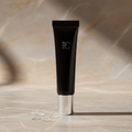 Sleek black Revision Skincare YouthFull Lip Replenisher tube on neutral warm gray marble – luxury beauty product photography