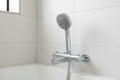 Minimalist professional handheld chrome shower head in modern white tile bath setting on slide bar