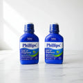 Clean studio composition of two blue digestive health liquid medicine bottles on white marble surface