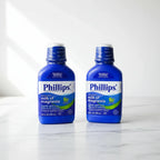 Clean studio composition of two blue digestive health liquid medicine bottles on white marble surface