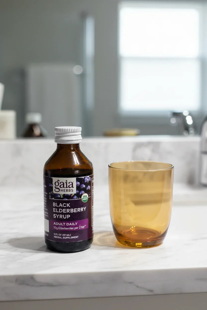 Gaia Herbs Black Elderberry Syrup amber bottle on white marble bathroom vanity next to amber drinking glass morning wellness