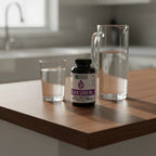Zhou Black Seed Oil bottle on dark-wood breakfast bar next to glass of water and modern glass water pitcher