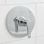 Close-up of American Standard Studio S polished chrome shower valve trim handle and round escutcheon plate on white tile.