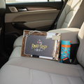 Inklings Paperie Kids Road Trip Kit activity box in the back seat of an SUV next to a colorful child's thermos showing real travel use
