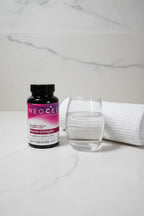 NeoCell Marine Collagen bottle on white quartz bathroom vanity next to rolled waffle-knit towel and apothecary glass of water