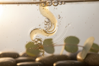 Close-up macro of clear bathwater with essential oil droplets swirling and tiny bubbles catching soft light