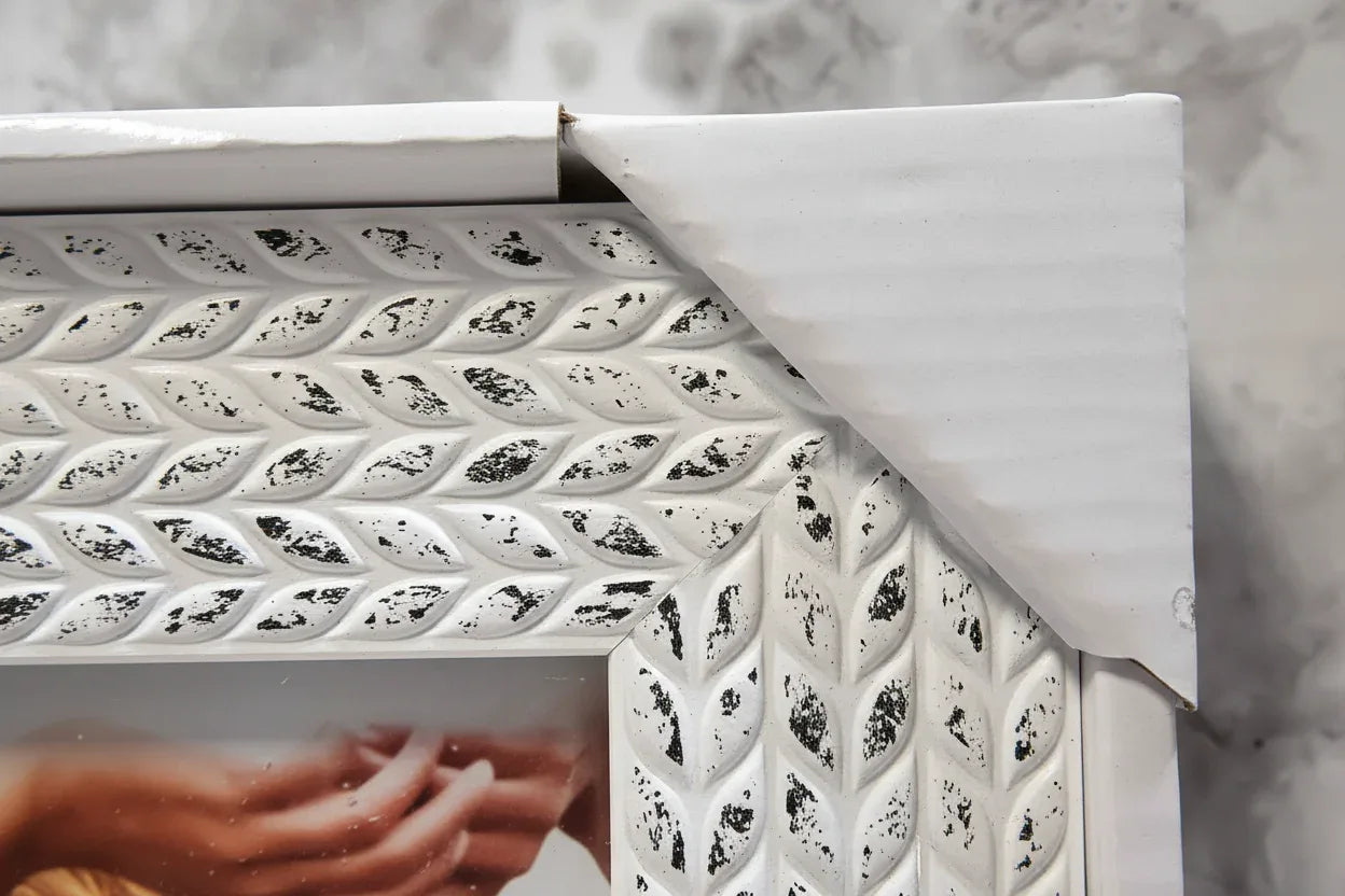 Macro texture focus showing white-on-dark distressing pattern and dimensional leaf relief on picture frame