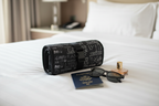 Mary Kay roll-up travel bag rolled compactly next to a passport, sunglasses, and perfume bottle on a hotel bed.