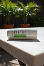 Clean white mineral sunscreen bottle resting on a bright outdoor patio table with soft natural light and green plants