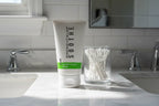 Clean bathroom vanity with Rodan + Fields SOOTHE Gentle Cream Wash tube on white marble beside cotton swabs