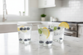 Clear glass tumblers on white marble countertop with sparkling water, fresh blueberries and lemon slice