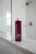 Rodan + Fields Volume+ Conditioner plum bottle on luxury marble shower ledge natural lighting