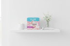 Minimalist white bathroom shelf with Gillette Venus Comfortglide White Tea refill box, white tea candle, white flowers, and Venus razor handle in soft natural light