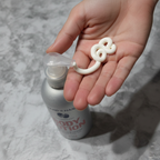 Rich white creamy lotion being dispensed from a pump bottle into a cupped hand in soft natural light