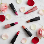 Flat lay of jewel-tone lipstick bullets in pink, red, mauve, and truffle on marble