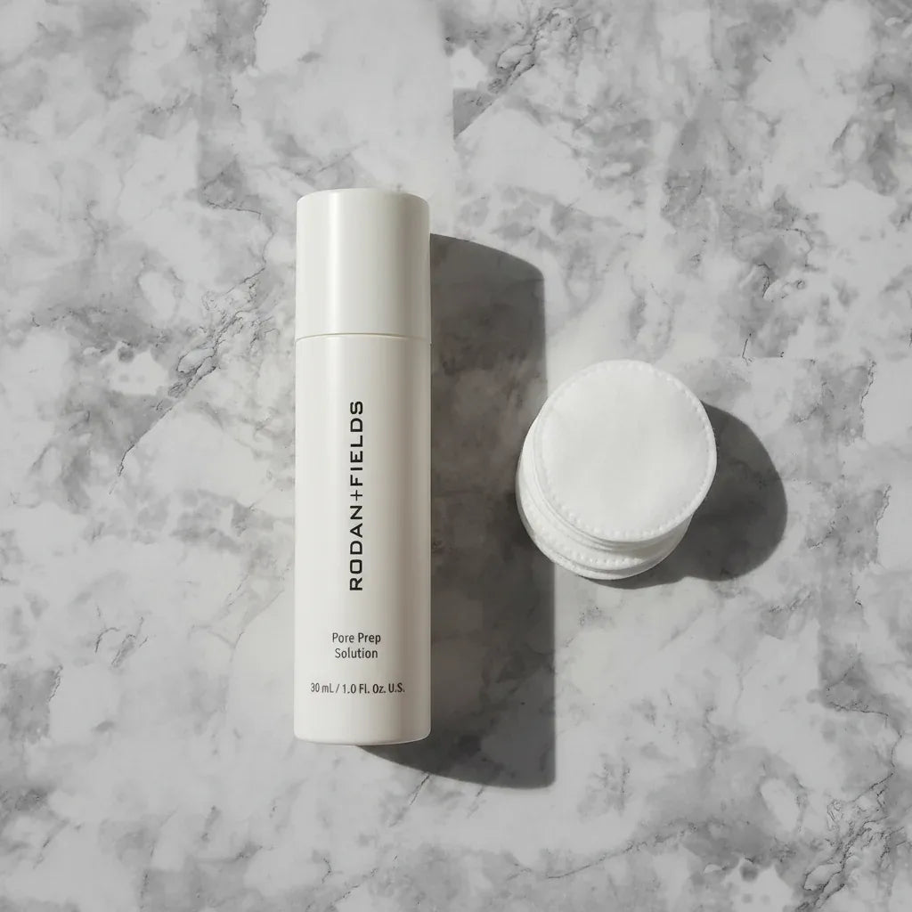 Top-down flat lay of Rodan + Fields Pore Prep Solution on white marble with cotton pads and soft daylight
