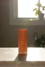Small orange high-end skincare serum bottle in warm morning sunlight casting soft shadows on white marble vanity