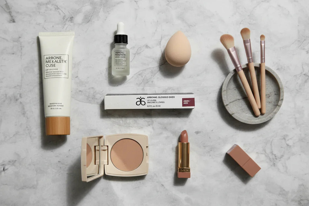 Arbonne Glossed Over Lip Gloss Anise organized makeup flat lay on stone countertop