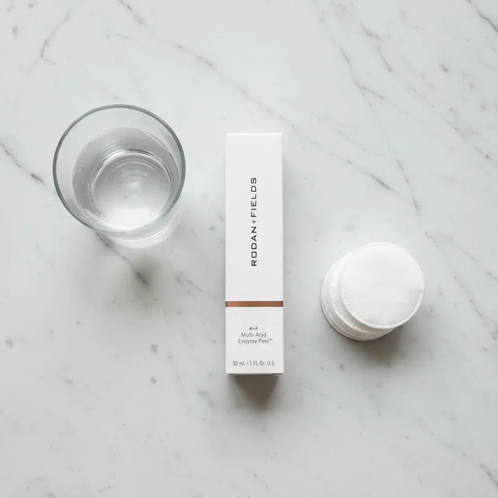 Top-down flat lay of Rodan + Fields peel box on marble with cotton rounds and glass of water