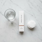 Top-down flat lay of Rodan + Fields peel box on marble with cotton rounds and glass of water