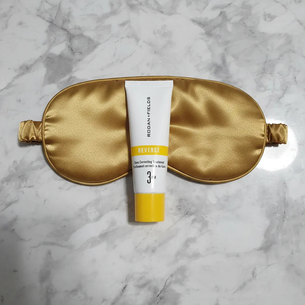 Top-down flat lay of Rodan + Fields REVERSE tube next to silk sleeping mask on marble surface