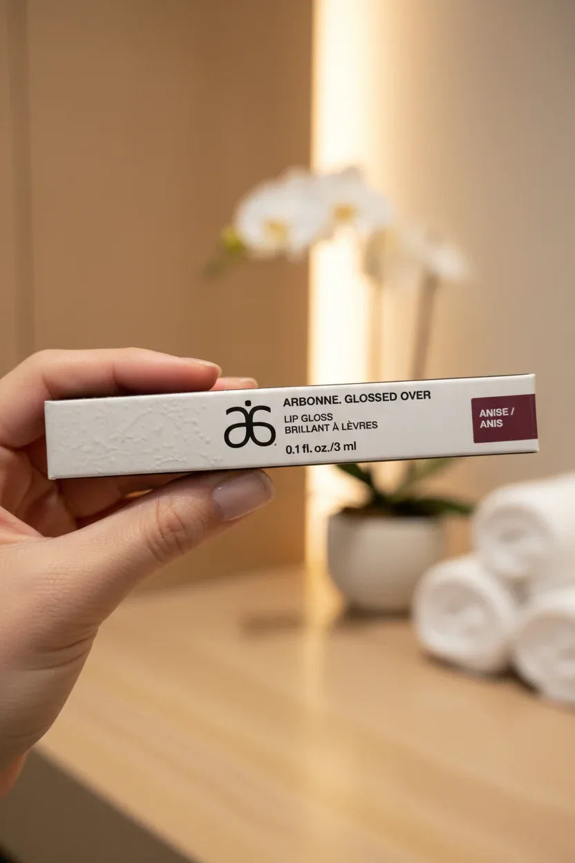 Arbonne Glossed Over Lip Gloss Anise in-hand close-up shallow depth of field spa background