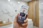 In-hand close-up of Bausch + Lomb LUMIFY Eye Illuminations metallic purple retail box against a neutral spa background