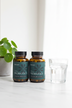 BIOMA Probiotics amber glass bottle on white marble surface with small green plant and glass of water