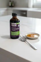 Gaia Herbs Black Elderberry Tonic on white quartz kitchen island next to silver teaspoon and dish of organic honey