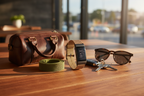 Smartwatch with tan woven perlon and green elastic bands beside travel bag and sunglasses on wooden surface – on-the-go lifestyle photography