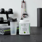 Sunwarrior Thermo Greens tub at workout station with shaker bottle, towel, and fitness accessories.