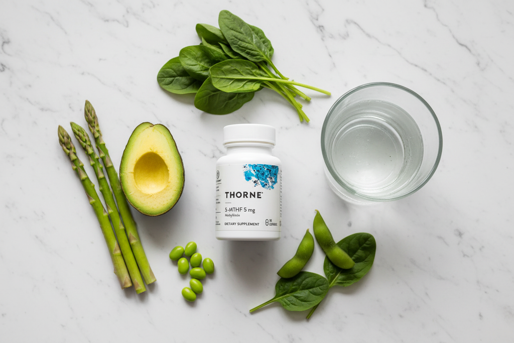 White supplement bottle on marble next to spinach, asparagus, and glass of water, folate wellness aesthetic