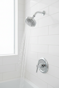 Moen Dartmoor polished chrome shower head installed on white tile bathroom wall with water flowing