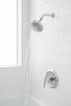 Moen Dartmoor polished chrome shower head installed on white tile bathroom wall with water flowing