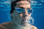 Swimmer underwater wearing blue competition swim goggles, clear water with bubbles