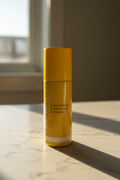 Morning light hitting a bright yellow skincare serum bottle on white marble countertop in warm golden natural lighting