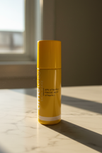 Morning light hitting a bright yellow skincare serum bottle on white marble countertop in warm golden natural lighting