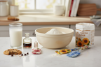 Cozy baking setup with floral print silicone spatulas, glass of milk, flour and mixing bowl on white counter