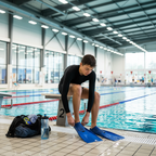 Young teen swimmer sitting at pool edge putting on swim training fins before practice