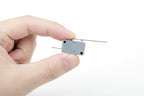 Hand holding a new gray OEM electrical microswitch component ready for appliance installation