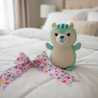 Squishmallows Hug Mees Mint Squirrel Plush displayed as gift on white bedding with colorful ribbon - More4less Outlet