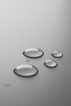 Minimalist clear hydration serum droplets on a smooth grey stone background in soft diffused lighting