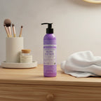 Dr. Bronner's Lavender Coconut Organic Hair Creme purple pump bottle on light-oak dresser near cosmetics organizer and soft white cotton hand towel