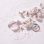 Lifestyle image - pink perfume bottle beside cherry blossom branches and flower petals on white marble, editorial beauty flatlay for visual context only