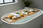 Spa-inspired bamboo tray across white soaking tub with towels sponges and botanical leaves in morning sunlight