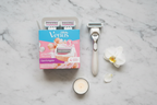 Elegant flatlay of Gillette Venus Comfortglide White Tea refill box with Venus razor handle, white tea candle, and white flower on marble surface